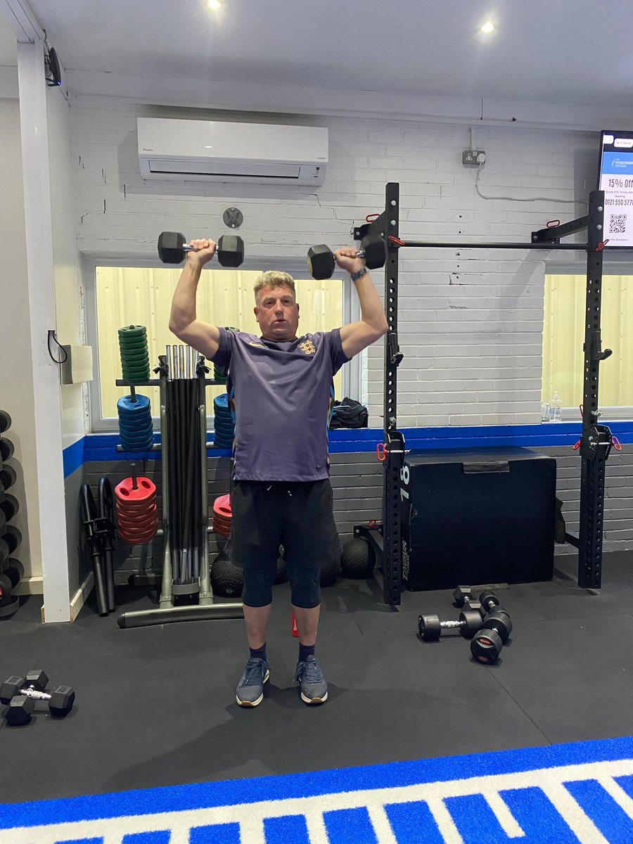 SPS Fitness male member doing dumbbell overhead press during a training session