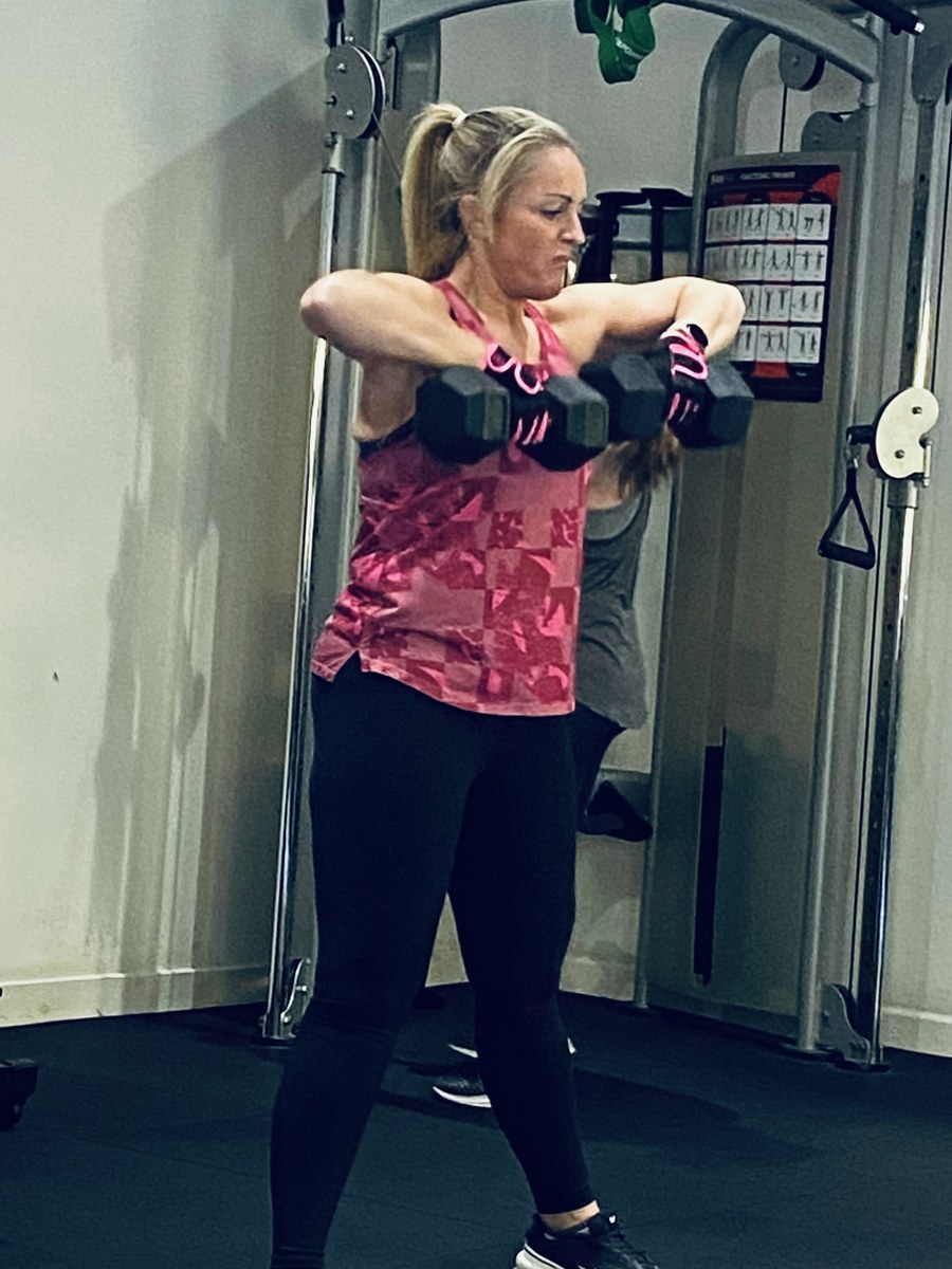 SPS Fitness member doing dumbbell raises with another member training behind her